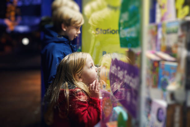 Petite fille qui colle son nez contre la vitrine d'un magasin de jouets