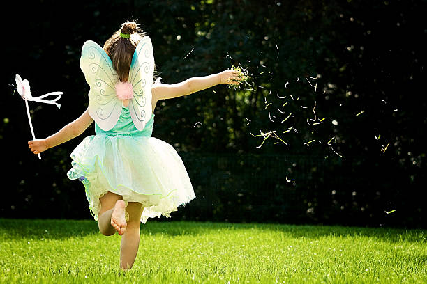 Petite fille qui court de dos dans l'herbe avec un déguisement de fée