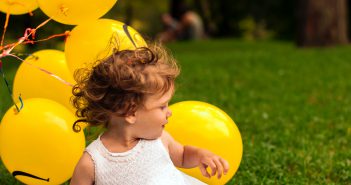 Petite fille en train de jouer dans l'herbe avec des ballons jaunes